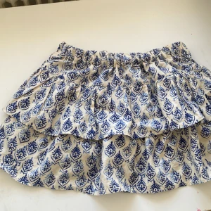 Vit och blå mönstrad kjol med volang - Säljer en söt vit kjol med blått bladmönster och volangdetalj. Kjolen är i storlek 134/140 men passar mig bara lite liten i midjan som har 158/164❤️❤️