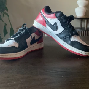 Nike Air Jordans Low svart/vit/röd - Säljer ett par Nike Air Jordans Low med svart, vit och röd färg. Skorna har klassisk snörning, rund tå och platt sula. Perfekta för dig som gillar streetwear och vill sticka ut med en ikonisk sneaker priset kan diskuteras.