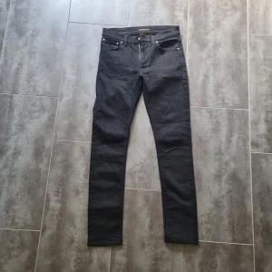 Svarta och gråa nudie Jeans  - Säljer 2 par svarta och gråa  jeans från Nudie Jeansco med klassisk femficksdesign och raka ben. Jeansen har silverfärgade nitar och knapp, samt normal passform. Perfekta för dig som gillar stilrena och tidlösa jeans.