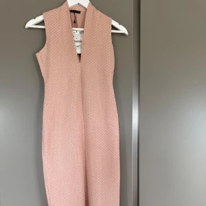 Ljusrosa ärmlös klänning från Zara - Säljer en ljusrosa ärmlös klänning från Zara med strukturerat tyg och djup v-ringning. Klänningen är slim/tight i passform och slits baktill för extra rörelsefrihet. Perfekt för dig som gillar stilrena och eleganta plagg.