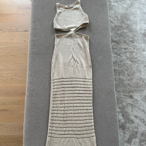 Beige stickad långklänning med cut-out från 4th & Reckless - Säljer en beige stickad långklänning från Aim'n med cut-out detaljer i midjan och hålmönster nedtill. Klänningen är ärmlös och har en tight passform som framhäver figuren. Perfekt för sommarens alla tillfällen!
