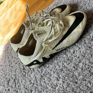 Nike Mercurial fotbollsskor i beige och svart - Säljer ett par Nike Mercurial fotbollsskor i beige med svarta detaljer och snörning. Skorna har en lätt och ventilerande ovandel samt platta dobbar för bra grepp på planen. Perfekta för dig som vill ha snabba och smidiga skor till match eller träning. Pris kan diskuteras 