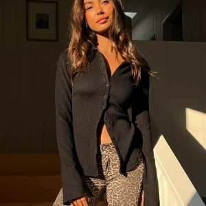 Svart ribbad skjorta - Säljer en stilren svart ribbad linneskjorta i tjockt material. Långa ärmar med slit på varsin ärm och knappar framtill. Använd 1 gång. I nyskick.