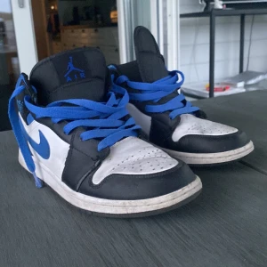 Blåa jordans - Säljer ett par Nike Air Jordans med svart, vit och blå färg. Skorna har blå snörning, blå swoosh och detaljer, samt klassisk rund tå och platt sula. Perfekta för dig som gillar streetwear och sneakers med attityd.