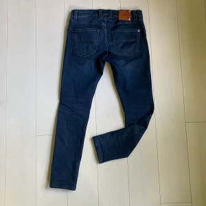 Mörkblå jeans från Tramarossa - Snygga mörkblå jeansbyxor från Tramarossa med silverfärgade knappar och röda sömdetaljer. Klassisk femficksmodell med diskret logga och personlig touch med initialer på myntfickan. Perfekta för dig som gillar stilrena jeans med unika detaljer. Modellen är Giotto. Nypris: ca 5000