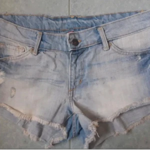 Ljusblå jeansshorts från H&M - Säljer ett par ljusblå jeansshorts från H&M med fransiga kanter och klassisk femficksdesign. Shortsen har låg midja och slitna detaljer framtill för en avslappnad look. Perfekta för varma dagar. Säljer då de var för stora för mig så bilderna är från tidigare ägare!💗