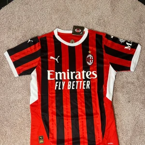 AC Milan hemmatröja Puma - Säljer en officiell AC Milan fotbollströja från Puma med klassiska röda och svarta ränder. Tröjan har korta ärmar, klubbmärke på bröstet och sponsortryck framtill. Perfekt för fans som vill visa sitt stöd på matchdagar.