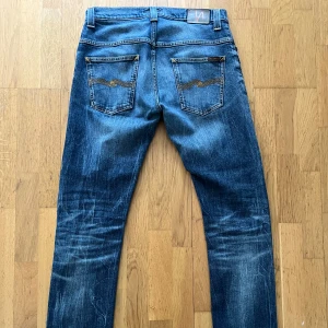 Blå jeans från Nudie Jeans - Unikt par Nudie jeans med snygga slitningar och fet tvätt. Storlek W32 L34. Bra skick med några slitningar som bara ger mer karaktär. Skriv gärna vid funderingar 