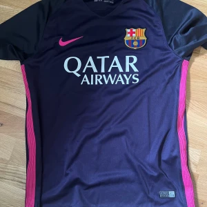 FC Barcelona Neymar Jr 11 bortatröja - Säljer en svart och rosa FC Barcelona bortatröja från Nike med Neymar Jr och nummer 11 på ryggen. Tröjan har korta ärmar, klubbmärke på bröstet och Qatar Airways som sponsortryck. Tillverkad i Dri-FIT material för bra komfort.