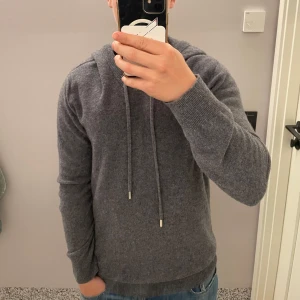 Merinoull tröja  - En mörkgrå hoodie i 100% merinoull. Tröjan är i en väldigt snygg mörkgrå färg, och i ett väldigt bekvämt material som är perfekt för avslappnade dagar. Den har en luva, samt två snören. Storlek S men skulle själv säga att den mer sitter som en M. Toppskick! Inte använd många gånger, och ser helt ny ut!