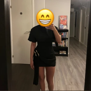 Svart kortklänning - Superfin svart klänning med en cool guld detalj på sidan. Säljer då den är förliten på mig (det är min kompis på bilden). Den har aldrig använts och prislappen sitter kvar. Skriv vid frågor! 🥰