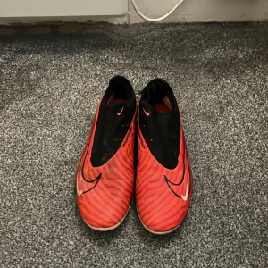 Nike Phantom fotbollsskor i rött och svart - Säljer ett par Nike Phantom fotbollsskor i rött och svart med vita detaljer. Dom är i helt okej skick men funkar endå bra. Säljer för dom är för små. Skriv vid fundering.