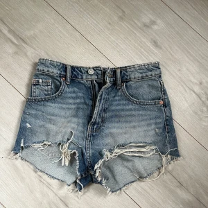 Blå jeansshorts från ZARA - Säljer ett par blå jeansshorts från ZARA med fransade kanter och slitna detaljer framtill. Går även att vika ner så de blir mer lågmidjade. Använda 1 gång så i princip nyskick!