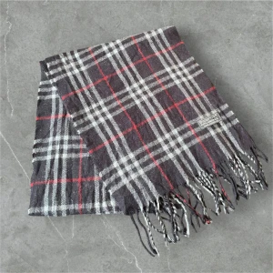 Rutig halsduk i ull från Burberry - Säljer en klassisk rutig halsduk från Burberry i mjuk ull. Nypris 4000 mitt pris 249🤩Halsduken har grå, vita och röda ränder samt fransar i ändarna. Perfekt accessoar för att lyfta din outfit.