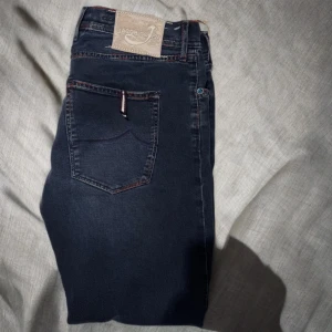 Jacob Cohen unika jeans - Unika jeans från Jacob Cohen med stitching i  rött, vitt och blått samt glänsande blå kristall knappar runtom på jeansen. Style 656.