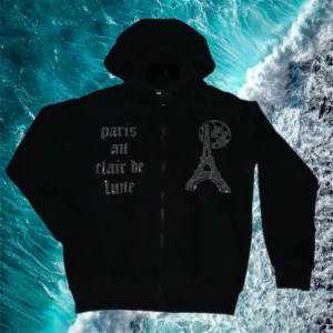 Svart zip up hoodie ifrån bling lucid  - Svart hoodie med dragkedja från Bling Lucid. På framsidan finns texten 'paris au clair de lune' i glittriga bokstäver och ett tryck av Eiffeltornet med måne. Perfekt för dig som gillar streetstyle och vill sticka ut.