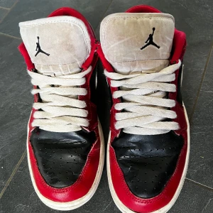 Nike Air Jordan 1 Low Chicago - Säljer ett par Nike Air Jordan 1 Low Chicago med klassisk röd, svart och vit färgkombination. Skorna har vit sula, svart tå och sidopanel, röda detaljer och vit swoosh. Ikonisk Jumpman-logga på plösen och Air Jordan-broderi på hälen.