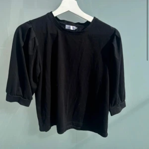 Svart topp med puffärm - En svart topp med rund halsringning och puffiga trekvartsärmar. Enkel och stilren design som passar till mycket. Tillverkad i mjukt bomullsmaterial för en bekväm känsla.