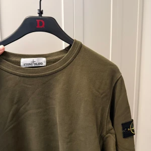 Olivgrön sweatshirt från Stone Island - Säljer en olivgrön sweatshirt från Stone Island med klassisk rund halsringning och logotyp-patch på vänster ärm. 