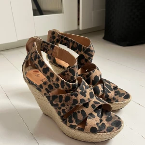 Leopardmönstrade kilklackssandaler från Ellos - Säljer ett par sandaler med hög kilklack från Ellos i leopardmönster. Skorna har flera breda remmar och dragkedja bak för enkel påtagning. Klacken är klädd i flätad jute för en somrig känsla. Lite fläckar på sulan, men inget som syns när skon är på. Skriv för fler bilder🤎