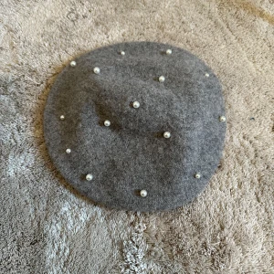 Grå basker med pärlor - Snygg grå basker dekorerad med pärlor. Klassisk rund form och tillverkad i mjukt ullmaterial. Köpt från Primark och använd fåtal gånger. 