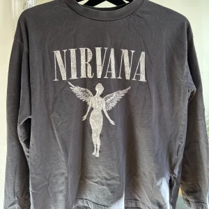 Långärmad tröja - Svart långärmad tröja med stort Nirvana-tryck och ängelmotiv på bröstet. Perfekt för dig som gillar bandmerch och vill ha en avslappnad stil.