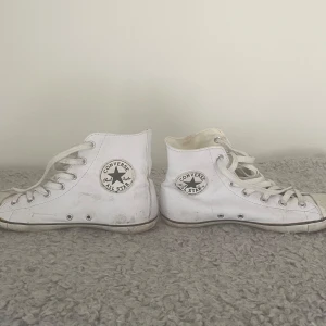 Vita Converse All Star high-top sneakers i skinn - Klassiska vita Converse All Star high-top sneakers med snörning och rund tå. Skorna har den ikoniska loggan på sidan och är tillverkade i skinn med gummisula. 