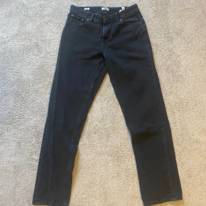 Svarta jeans från Jack & Jones - Säljer ett par svarta jeans från Jack & Jones. Klassisk femficksmodell med raka ben och normal passform. Jeansen har knapp och dragkedja i gylfen samt bälteshällor i midjan. Perfekta för en stilren vardagslook.