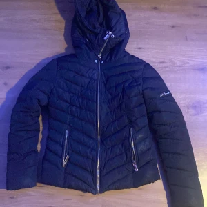 Svart pufferjacka från Roco Baroco - Säljer en svart pufferjacka från Roco Baroco med huva och dragkedja framtill. Jackan har två snedställda fickor med dragkedja och quiltad design. Perfekt för kyligare dagar och riktigt snygg passform. 