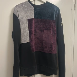 Patchwork tröja i sammet från Vichy - Unik långärmad tröja från Vichy i patchwork-stil med sammetspaneler i svart, grått och vinrött. Tröjan har rund halsringning och en cool badge på ena ärmen. Tröjan är ganska liten i storleken så skulle rekommendera den för dom med M istället för L