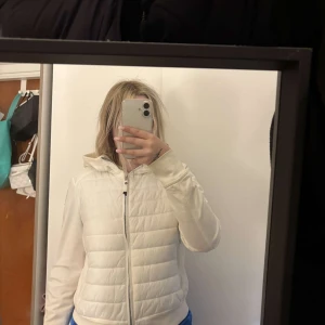 Vit quiltad pufferjacka med huva från Parajumpers - Säljer en vit quiltad pufferjacka från Parajumpers med huva och dragkedja framtill. Jackan har en klassisk passform och en broderad logotyp på ärmen. Perfekt för kyligare dagar och enkel att matcha med olika outfits.