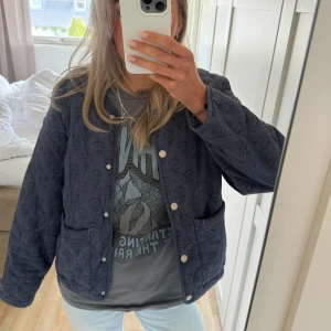 Mörkblå quiltad jacka med knappar - Säljer en mörkblå quiltad jacka med rund halsringning och stora fickor framtill. Jackan har tryckknappar och ett diskret mönster i tyget. Så snygg till allt❣️❣️