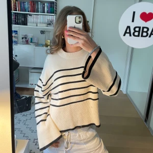 Randig stickad tröja  - Säljer en stickad, oversized tröja från Gina Tricot i vitt med svarta ränder. Tröjan har lång ärm, bred ribbad kant vid halsen och slitsar i sidorna. Perfekt för en avslappnad och trendig look.