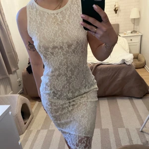 Vit spetsklänning med blommönster - Säljer en vit, tight spetsklänning med blommigt mönster. Klänningen är ärmlös och har en rund halsringning samt en fin detalj med nyckelhålsöppning i ryggen. Perfekt för sommarens tillfällen!