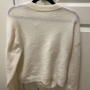 Vit stickad tröja från H&M - Säljer en enkel och stilren vit stickad tröja från H&M. Tröjan har rund halsringning, långa ärmar och ribbade muddar vid hals, ärmslut och nederkant. Perfekt för lager-på-lager under kyliga dagar.