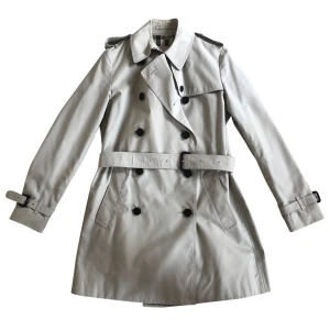 Beige trenchcoat från Burberry - Klassisk beige trenchcoat från Burberry med dubbelknäppning, bälte i midjan och axelklaffar. Jackan har ikoniskt rutigt foder. Perfekt för dig som vill ha en tidlös och stilren look. Bra skick, kemtvättad, stl 38-40.