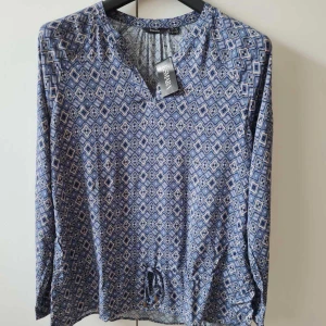 Långärmad blus från Esmara strl 44 - Säljer en blå långärmad blus från Esmara med geometriskt mönster i vitt och beige. Blusen har knytning nertill och är tillverkad i mjuk 100% viskos. Storlek 44. Kan hämtas i Vallentuna.