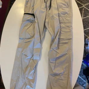 Beiga cargobyxor från H&M - Säljer ett par beiga cargobyxor från H&M med relaxed fit. Byxorna har flera stora fickor på sidorna och resår i midjan med snörning. 