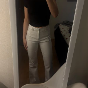 Vita bootcut byxor - Säljer ett par vita bootcut byxor med hög midja. Byxorna har en klassisk passform och stängs med dragkedja och knapp framtill. Perfekta att styla med en enkel topp eller skjorta.