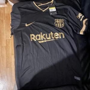 FC Barcelona svart fotbollströja Nike - Snygg svart FC Barcelona matchtröja från Nike med guldiga detaljer och loggor. Rakuten och UNICEF tryck, La Liga-märke på ärmen och klassisk klubbsköld på bröstet. Dri-FIT material för bästa komfort.