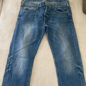 Blå Lee jeans Daren - Säljer ett par klassiska blå jeans från Lee, modell Daren. Jeansen har fem fickor, normal passform och raka ben. Snygga slitningar framtill och Lee-lapp bak i midjan. Storlek W36 L34.