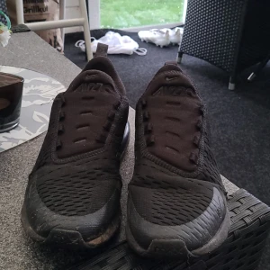 Svarta Nike Air Max 270 sneakers - Säljer ett par helsvarta Nike Air Max 270 sneakers med luftig mesh och tydlig Air Max-dämpning i hälen. Skorna har rund tå, platt sula och diskret Nike-logga på sidan. Perfekta för dig som gillar sportig och stilren look. Dem har några hål men det går att använda samt lite luft i sulan