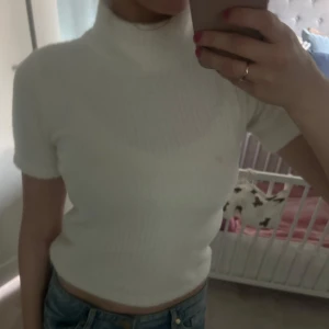 Vit ribbad kortärmad topp - Säljer en vit ribbad topp med korta ärmar och hög hals. Toppen är figurnära och har en enkel, stilren design som passar till mycket. Perfekt att matcha med jeans eller kjol. Jätteskönt material