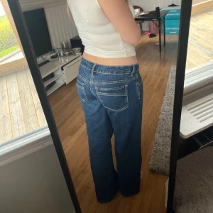 Blå raka jeans - Säljer ett par klassiska blå jeans med raka ben och normal passform. Jeansen har fem fickor, synliga sömmar och stängs med dragkedja och knapp. Perfekta till vardags och lätta att matcha med olika toppar.