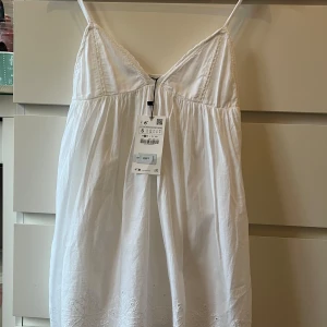 Vit sommarklänning  - Söt vit miniklänning från Zara med tunna axelband och v-ringad hals. Klänningen har broderade detaljer längst ner. Klänningen är mycket kort.