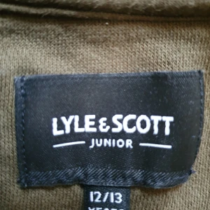 Olivgrön hoodie från Lyle & Scott Junior - Säljer en olivgrön hoodie från Lyle & Scott Junior med dragkedja vid halsen, magficka och bröstficka. Tröjan har långa ärmar och är tillverkad i bomull och polyester. Perfekt för en avslappnad stil. Mycket snygg och gosig, och i gott skick då hen hade mkt annat att välja bland under perioden då denna passade...