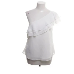 Vit oneshoulder volangtopp från Bubbleroom - Säljer en vit oneshoulder topp från Bubbleroom by Carolina Gynning. Toppen har dubbla volanger längs axeln och är tillverkad i ett lätt, luftigt material. Perfekt för dig som vill ha en stilren och trendig look.