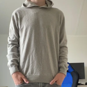 Biege hoodie i kashmir från Oscar Jacobson - Säljer en stilren ljusgrå hoodie från Oscar Jacobson i mjuk kashmir. Tröjan har lång ärm, ribbade muddar och klassisk huva. Perfekt för dig som gillar en enkel och lyxig look. Passar till mycket och är superbekväm. Nypris 1500!