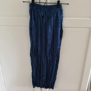 Marinblå plisserade kjol från Zara - Säljer marinblå plisserade kjol från Zara med resår i midjan. Kjolen är tillverkade i ett glansigt syntetmaterial. Perfekta för dig som vill ha en bekväm och trendig look.                                                                    Produkt mått: Midja; 25cm, längd; 84,5cm 