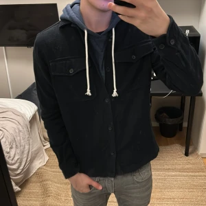 Svart overshirt från Jack & Jones - Säljer en snygg svart overshirt från Jack & Jones i storlek M. Den har en stilren design med knappar framtill och två bröstfickor. Perfekt för höst och vår, och funkar både till vardags och fest. Passar bra över en hoodie för en avslappnad look.